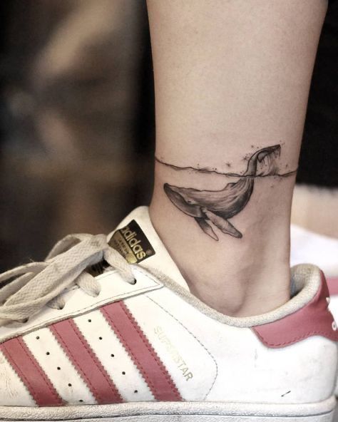 Hình xăm cá voi mini phong cách blackwork ở mắt cá chân, chi tiết rõ nét.