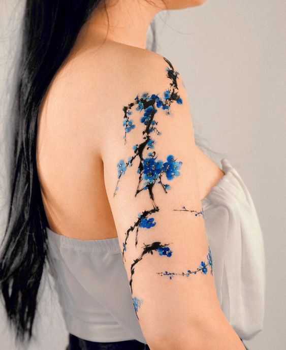 Hình xăm hoa đào xanh thật nổi bật Hình xăm hoa xanh phong cách màu nước trên cánh tay, chi tiết tinh tế, độ phân giải cao.