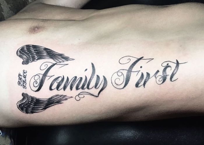 Hình xăm chữ "Family First" với đôi cánh trên ngực, phong cách blackwork, ảnh HD.