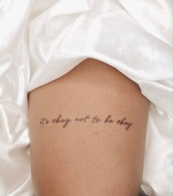 Hình xăm chữ "It's okay not to be okay" trên đùi, phong cách tối giản, độ phân giải HD.