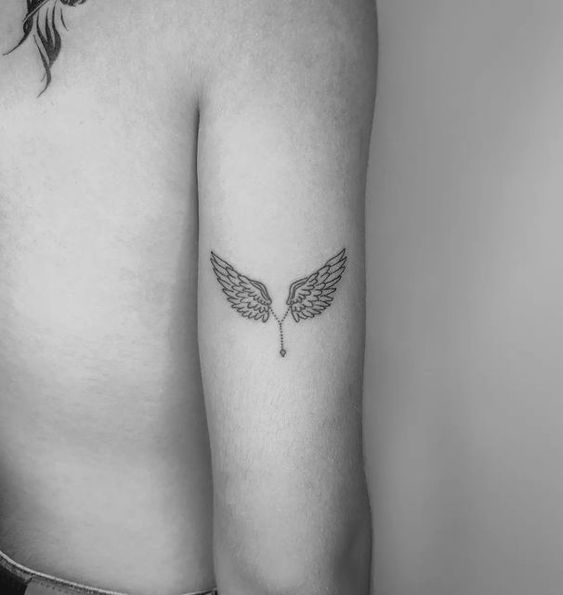 Hình xăm cánh thiên thần mini trên bắp tay, phong cách blackwork, chi tiết rõ nét, độ phân giải HD.