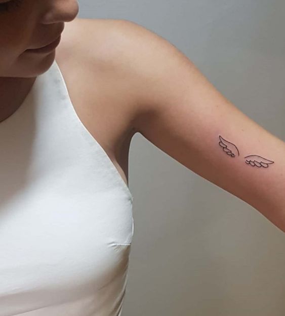 Hình xăm mini cánh thiên thần ở bắp tay, phong cách blackwork đơn giản, ảnh độ phân giải HD.