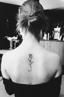 Hình xăm hoa hồng mini sau lưng, phong cách blackwork, ảnh đen trắng, độ chi tiết cao.