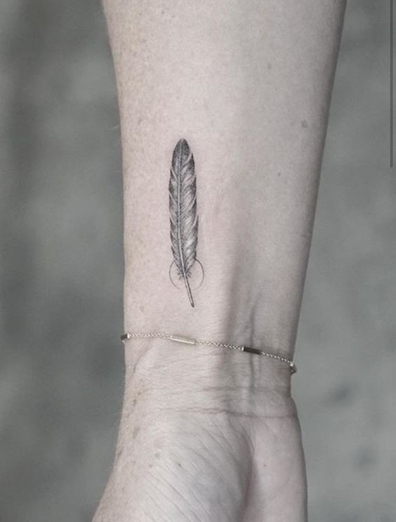 Hình xăm lông vũ mini trên cổ tay, phong cách blackwork, chi tiết rõ nét, ảnh HD.