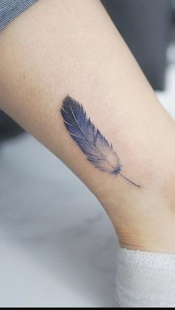 Hình xăm lông vũ mini trên mắt cá chân, phong cách màu nước, chi tiết rõ nét, độ phân giải cao.