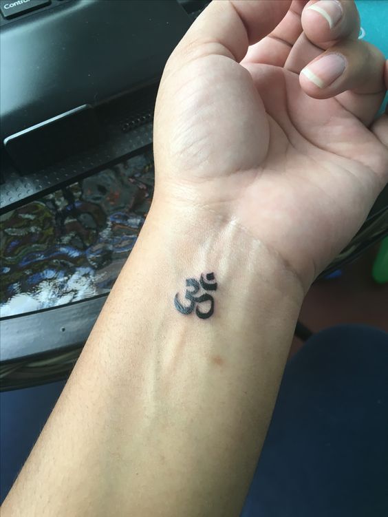 hình xăm chữ om mini ở cổ tay Hình xăm ký tự Om trên cổ tay, phong cách blackwork, chi tiết đơn giản, ảnh HD.