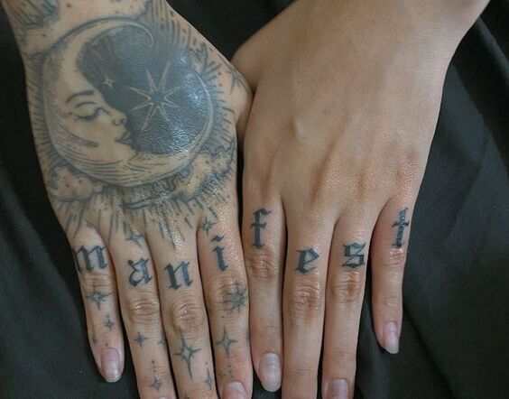 Hình xăm mặt trăng và chữ "manifest" trên tay, phong cách blackwork, chi tiết sắc nét.