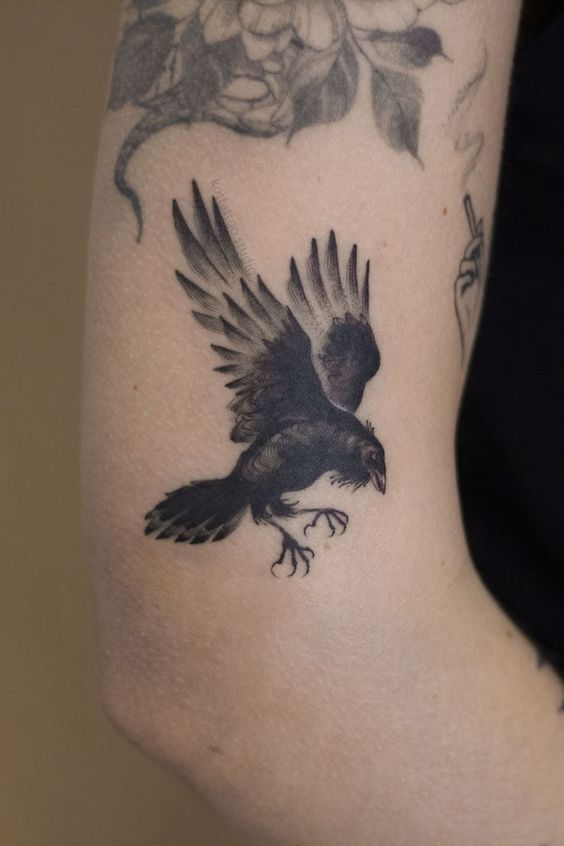 Hình xăm chim quạ phong cách blackwork trên cánh tay, chi tiết rõ nét, độ phân giải HD.