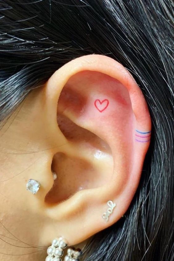 hình xăm trái tim đỏ nhỏ nhắn trên tai Hình xăm mini trái tim và đường kẻ màu trên tai, phong cách minimalist, ảnh HD chi tiết.