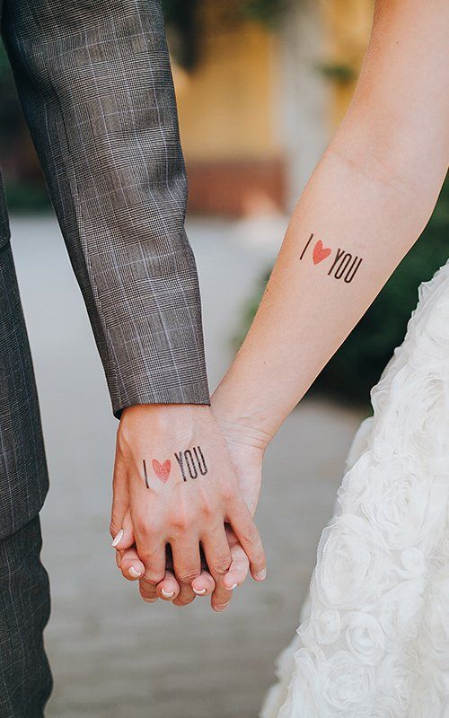 Hình xăm chữ "I ♥ You" trên cánh tay, phong cách tối giản, ảnh HD, đôi tay nắm nhau trong khung cảnh tự nhiên.