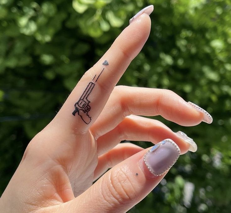 mẫu hình xăm cây súng nhỏ nhắn ở ngón trỏ Hình xăm súng mini trên ngón tay, phong cách blackwork tinh tế, ảnh chụp HD sắc nét.