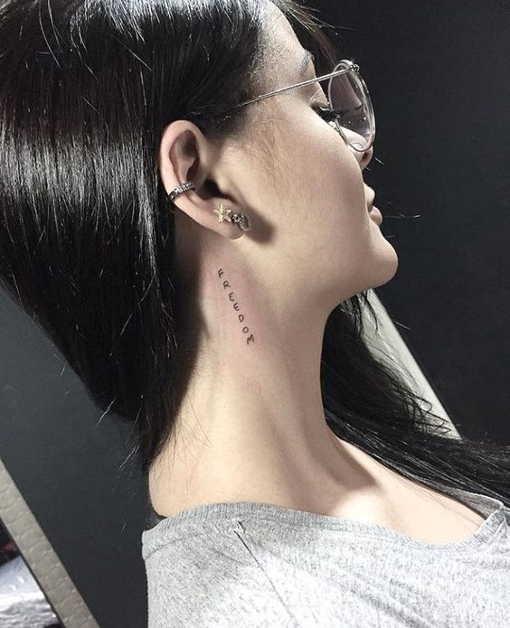 Hình xăm chữ "freedom" sau tai, phong cách tối giản, ảnh HD rõ nét.