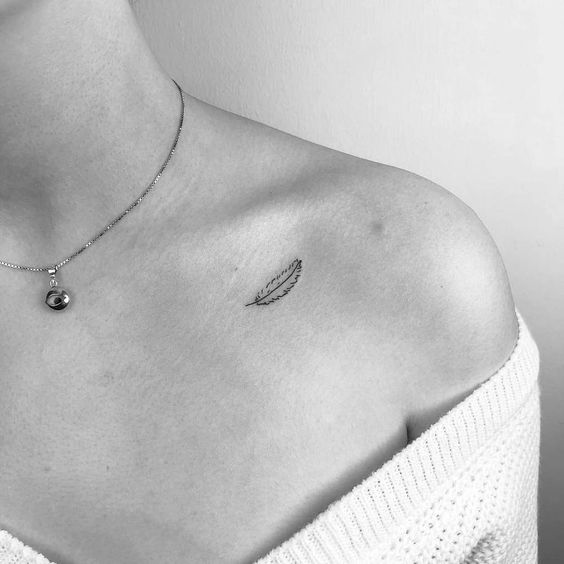 Hình xăm lông vũ mini trên vai, phong cách blackwork, ảnh đen trắng, chi tiết rõ nét.