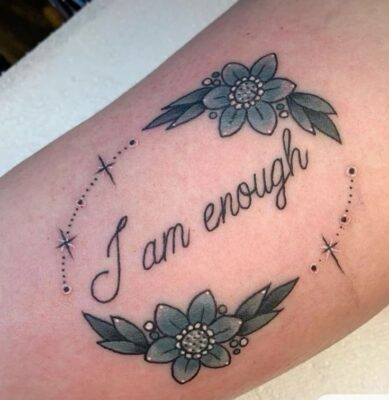 Hình xăm chữ "I am enough" với hoa xanh, phong cách blackwork trên cánh tay, ảnh HD rõ nét.