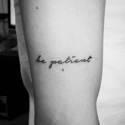 Hình xăm chữ "be patient" trên tay, phong cách chữ viết tay, ảnh đen trắng, độ phân giải HD.