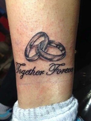 Hình xăm nhẫn đôi và chữ "Together Forever" trên chân, phong cách blackwork, chi tiết rõ nét, độ phân giải HD.
