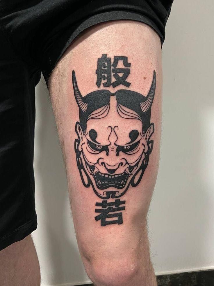 Hình xăm mặt quỷ phong cách blackwork ở đùi, chi tiết rõ nét, độ phân giải HD.