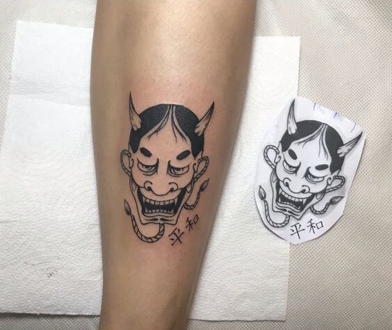Hình xăm mặt nạ Oni đen trắng trên chân, phong cách blackwork, chi tiết rõ nét, độ phân giải HD.