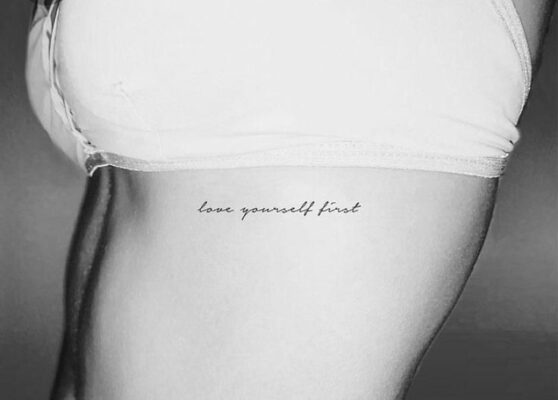 Hình xăm chữ "love yourself first" trên eo, phong cách tối giản, ảnh đen trắng, độ phân giải HD.