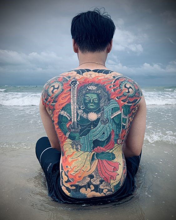 Hình xăm thần trên lưng, phong cách màu sắc, chi tiết sống động, độ phân giải HD, chụp ở bãi biển.