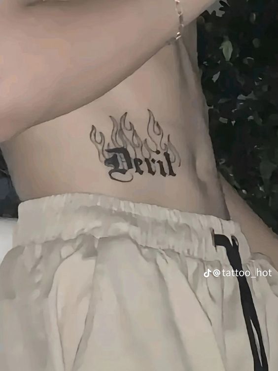 Hình xăm chữ "Devil" với ngọn lửa ở mạn sườn, phong cách blackwork, chi tiết rõ nét, ảnh chất lượng HD.