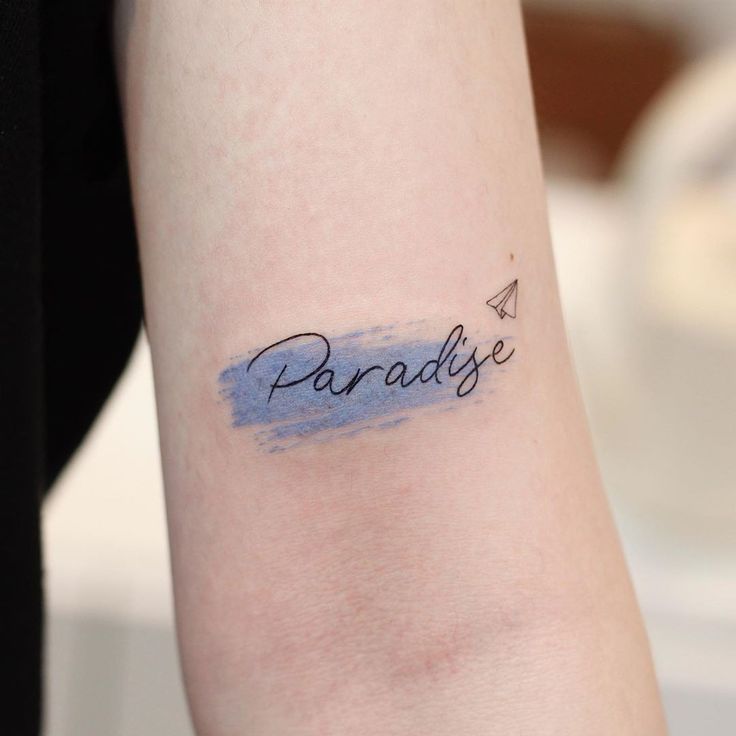 Hình xăm chữ "Paradise" phong cách màu nước trên tay, chi tiết nhẹ nhàng, độ phân giải HD.