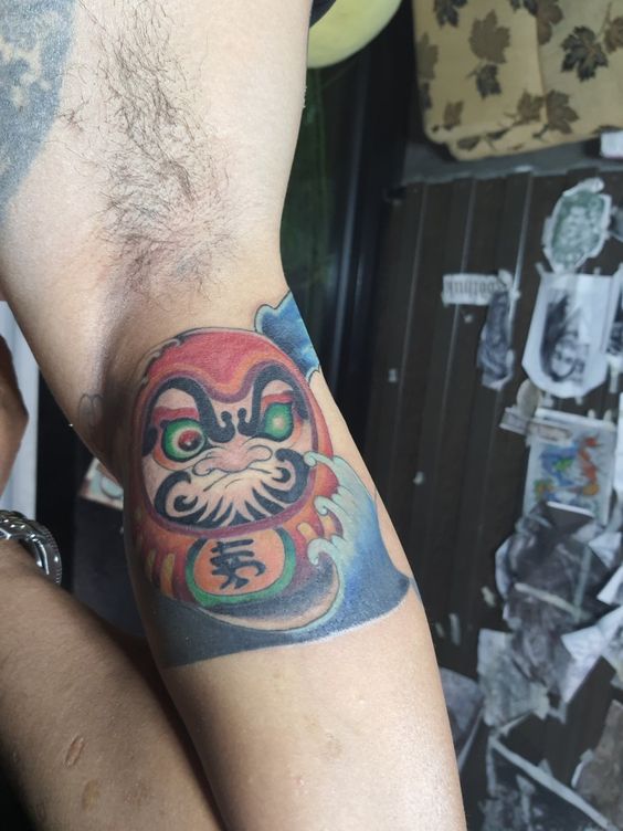hình xăm của anh khách mặt daruma trên bắp tay siêu ngầu Hình xăm Daruma đầy màu sắc trên bắp tay, phong cách truyền thống Nhật Bản, độ chi tiết cao, ảnh HD.