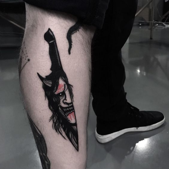 Hình xăm dao và mặt quỷ phong cách blackwork trên bắp chân, chi tiết sắc nét, độ phân giải HD.