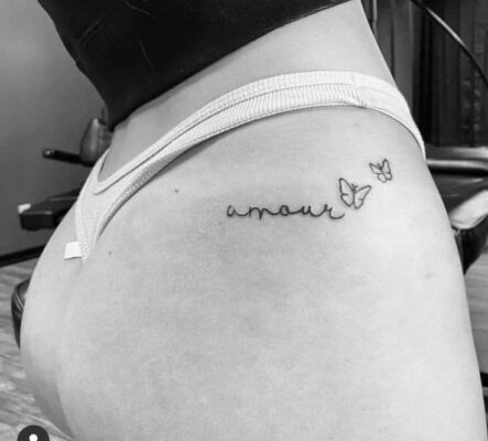 Hình xăm chữ "amour" và bướm nhỏ trên hông, phong cách tối giản, ảnh đen trắng, độ phân giải HD.