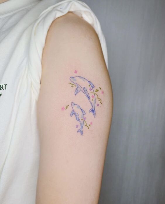 Hình xăm thể hiện tình cảm gia đình Hình xăm cá heo mini trên cánh tay, phong cách màu nước, chi tiết tinh tế, độ phân giải HD.