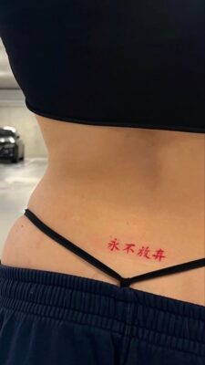 Không bao giờ bỏ cuộc - Thể hiện ý chí quyết tâm Hình xăm chữ đỏ ở eo phong cách tối giản, độ phân giải HD, ảnh tập trung vào chi tiết hình xăm.