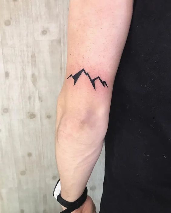 Hình xăm núi tối giản, phong cách blackwork trên cánh tay, chi tiết rõ nét, độ phân giải HD.