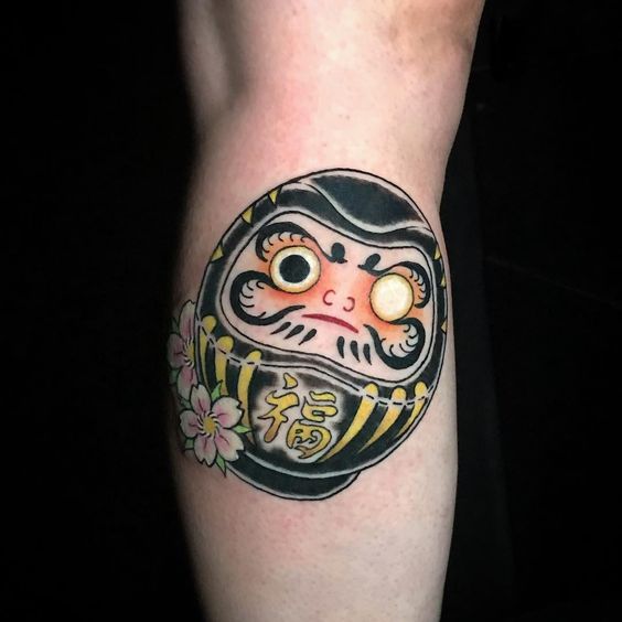 thiết kế xăm daruma mặt tròn màu đen với hoa anh đào nổi bật Hình xăm Daruma truyền thống trên cánh tay, phong cách màu sắc, chi tiết rõ nét, độ phân giải HD.