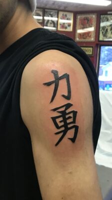 mang thông điệp " mạnh mẽ và dũng cảm " Hình xăm chữ Trung Quốc trên bắp tay, phong cách blackwork, chi tiết rõ nét, ảnh HD.