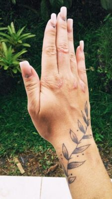 Hình xăm cành lá trên cổ tay, phong cách blackwork chi tiết, nền xanh tự nhiên, ảnh HD.