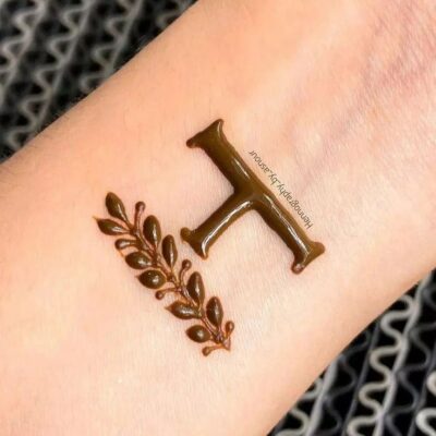 Hình xăm chữ T và nhánh lá trên cổ tay, phong cách henna, chi tiết rõ nét, độ phân giải HD.