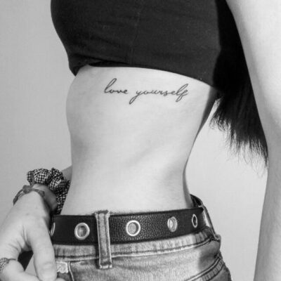 Hình xăm chữ "love yourself" trên eo, phong cách tối giản, ảnh đen trắng, độ phân giải HD.