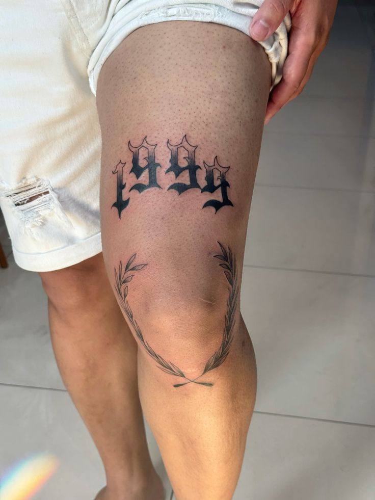 Hình xăm số 1999 và vòng nguyệt quế trên đùi, phong cách blackwork, chi tiết rõ nét, độ phân giải HD.