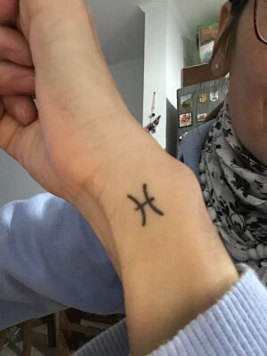 Hình xăm cung Song Ngư mini trên cổ tay, phong cách blackwork, ảnh rõ nét.