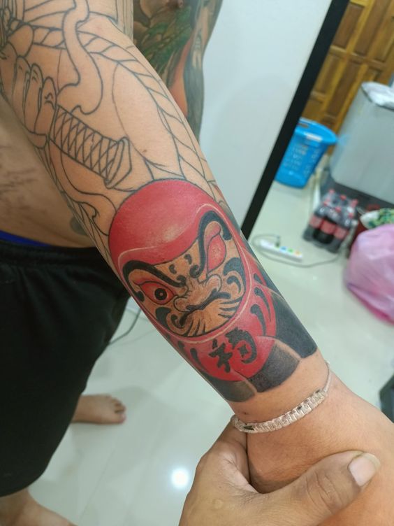 mẫu xăm daruma trên cổ tay cho anh khách siêu chất chơi Hình xăm Daruma màu sắc trên cánh tay, phong cách truyền thống, chi tiết rõ nét, độ phân giải HD.