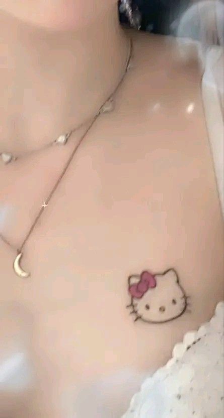 Hình xăm mini nhân vật mèo trên ngực, phong cách màu sắc, độ nét cao.