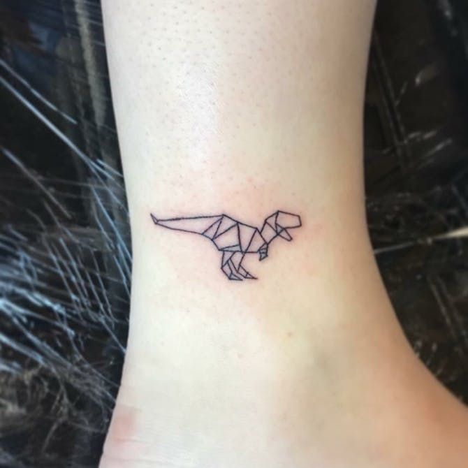 Hình xăm khủng long origami mini trên mắt cá chân, phong cách blackwork, chi tiết tinh tế, ảnh HD.