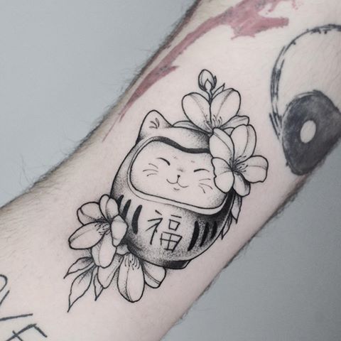 mẫu xăm mèo thần tài daruma cầu tài lộc Hình xăm búp bê Daruma và hoa trên tay, phong cách blackwork chi tiết, ảnh HD.