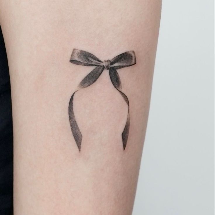 Kiểu xăm nơ màu đen Hình xăm nơ mini trên cánh tay, phong cách blackwork, chi tiết rõ nét, ảnh HD.