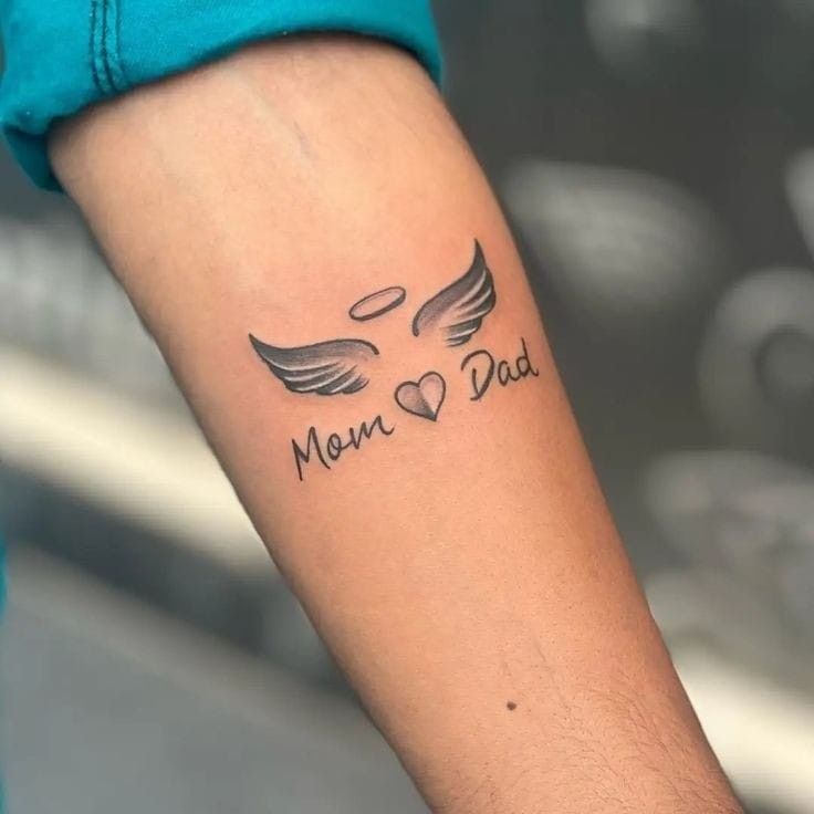 Hình xăm chữ "Mom Dad" với cánh thiên thần trên tay, phong cách blackwork, chi tiết rõ nét, ảnh HD.