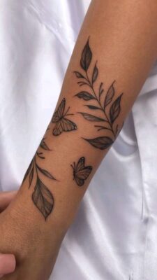 Hình xăm bướm và lá trên cánh tay, phong cách blackwork, chi tiết tinh tế, ảnh HD.