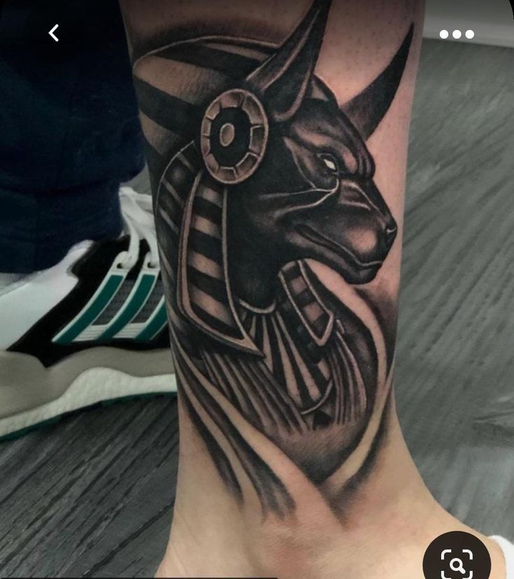 Hình xăm Anubis phong cách blackwork trên chân, chi tiết sắc nét, độ phân giải HD.