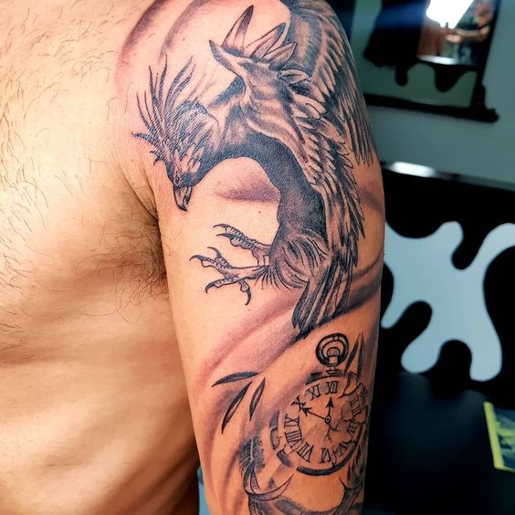 Tattoo chim phượng hoàng trên bắp tay của anh khách Hình xăm phượng hoàng và đồng hồ trên bắp tay, phong cách blackwork, chi tiết rõ nét, độ phân giải HD.