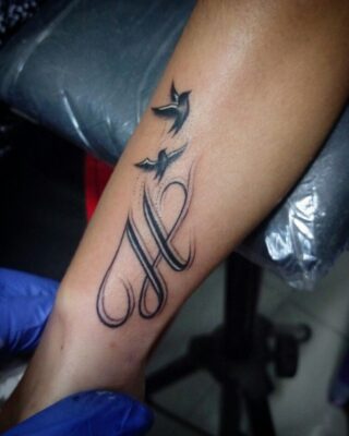 Hình xăm chữ và chim trên cánh tay, phong cách blackwork, chi tiết rõ nét, độ phân giải HD.