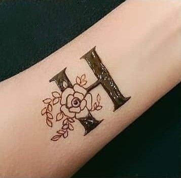 Hình xăm chữ H và hoa trên cánh tay, phong cách blackwork tinh tế, độ phân giải HD.